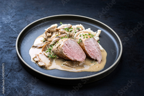 Modern style traditional barbecue Iberian pork filet medaillons in cream sauce with mushrooms and herbs offered as close-up on a Nordic design plate with copy space