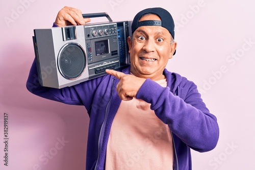 Senior handsome grey-haired modern man listening to music using vintage boombox smiling happy pointing with hand and finger