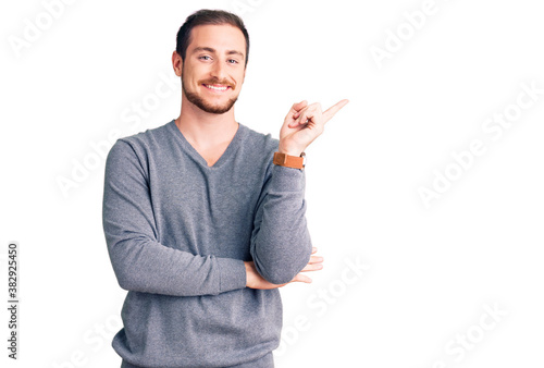 Young handsome caucasian man wearing casual winter sweater smiling happy pointing with hand and finger to the side
