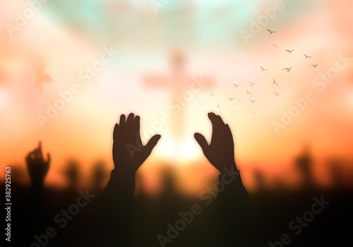 Resurrection of Easter Sunday concept: Silhouette christian people hand rising over blurred cross on spiritual light background