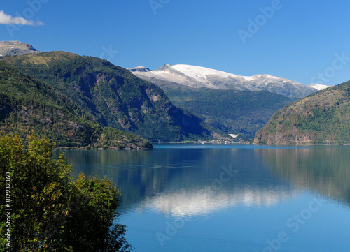View From Urnes To The Lustrafjord And A Village On A Sunny Summer Day With A Clear Blue Sky And A Few Clouds