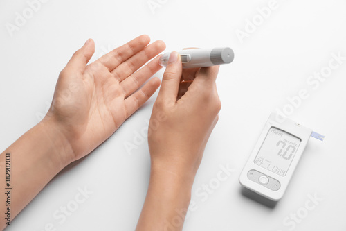 Female hands with lancet pen and glucometer on white background. Diabetes concept