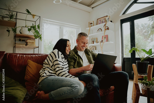 Young couple sitting on the couch looking at a laptop - 2 people streaming from their laptop