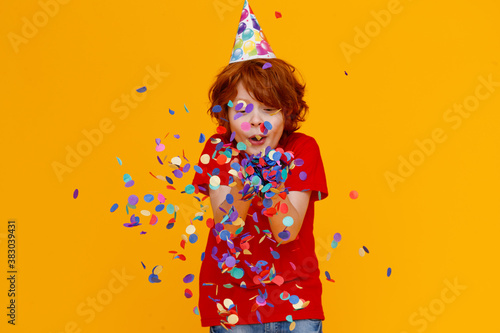 happy birthday! ginger child boy with confetti on yellow background