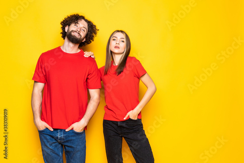 Portrait of content couple in basic clothing smiling at camera while woman putting her head on male shoulder over yellow background