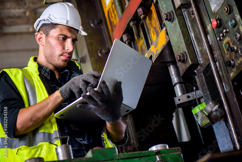 Caucasian engineer mechanic man checking for maintenance pressing metal machine by laptop at factory, worker at industrial concept