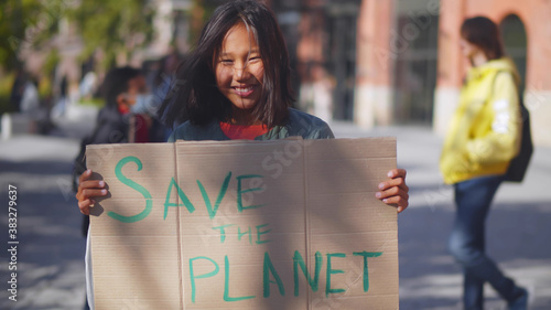 Portrait of asian schoolgirl showing sign with save the planet text protesting against pollution