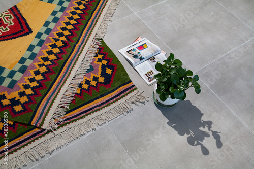 A hand woven and knotted Persian colorful kilim on the floor with magazines and flower pot 