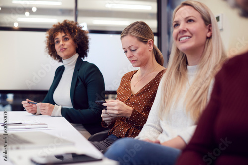 Businesswoman Looking At Mobile Phone During Presentation By Colleague In Modern Office