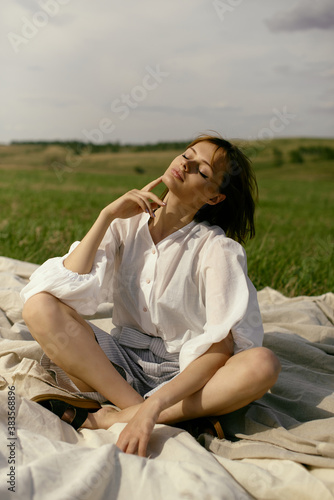 Nice picnic on the grass. Young beautiful woman in the middle of green field. Summer landscape, good weather. Windy day with sun and clouds. Cotton white suit eco style. 