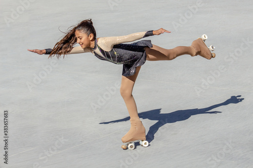 Teenage girl's back shot performing a figure skating on wheels. Pigeon figure