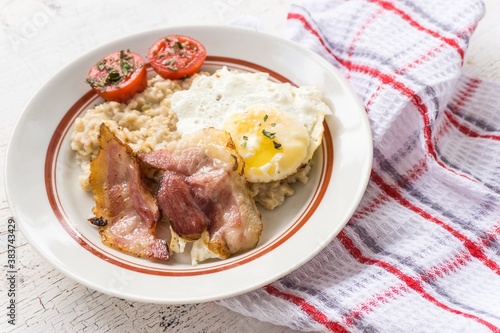 English breakfast with oatmeal, bacon, scrambled eggs and tomatoes.