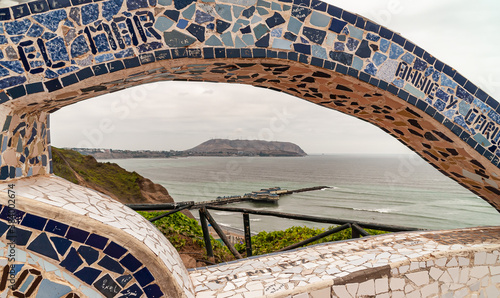 Miraflores, Peru - December 4, 2008: Parque del Amor, Love Park. Gray-green Pacific Ocean with Pier and mountainous coastline visible under art faience bow of stone. Some green foliage. 