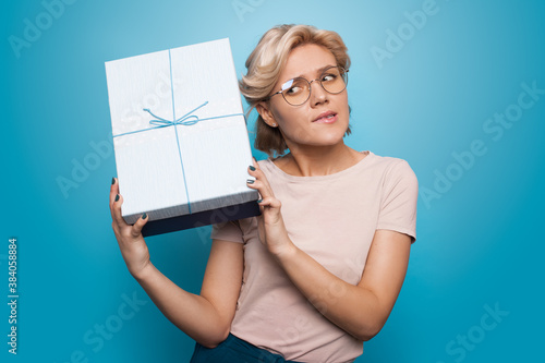 Blonde caucasian woman listening to her present gesturing impatience on a blue studio wall