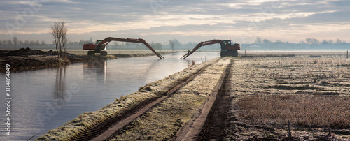 Dredging of an inland canal by cranes in winter at sunset. 