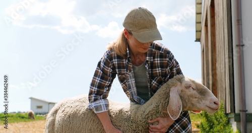 Caucasian pretty young woman shepherd holding sheep and petting it outdoors. Beautiful female farmer caressing and stroking animal. Livestock farming concept. Outdoors.