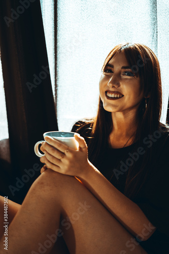 Chica joven en bikini lencería y pijama en su habitación con luz entre las cortinas oscuras de ambiente con café y haciendose selfies