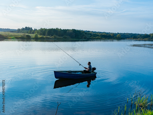 Elderly man fishing with a rod on a small fishing boat on the lake 