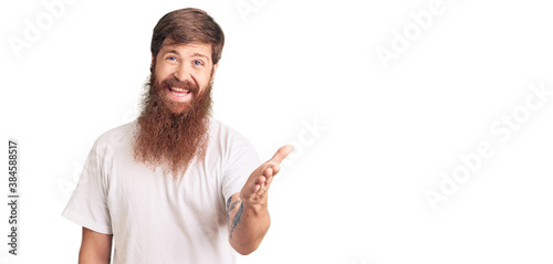 Handsome young red head man with long beard wearing casual white tshirt smiling friendly offering handshake as greeting and welcoming. successful business.
