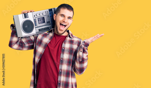 Young handsome man listening to music holding boombox celebrating victory with happy smile and winner expression with raised hands