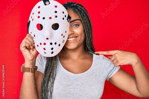 Young african american woman with braids wearing hockey mask pointing finger to one self smiling happy and proud