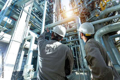 Industrial engineer or worker checking pipeline at oil and gas refinery plant form industry zone with sunrise and cloudy sky, oil and gas Industry concept.