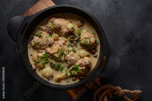 Fricassee - French Cuisine. Chicken stewed in a creamy sauce with mushrooms in a black dutch oven on a black table 