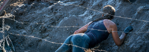 Sexy athlete crawling in mud under barbed wire at an obstacle course race