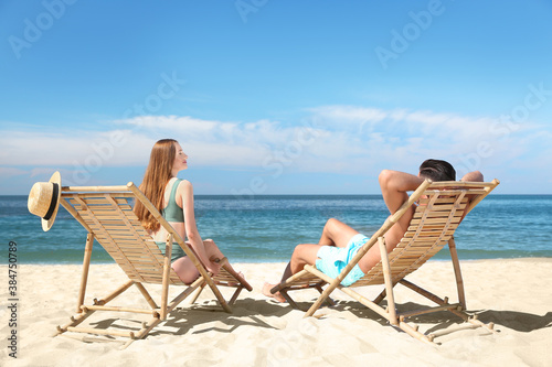 Woman in bikini and her boyfriend on deck chairs at beach. Lovely couple