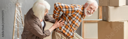 panoramic shot of senior man suffering from backache while wife trying help