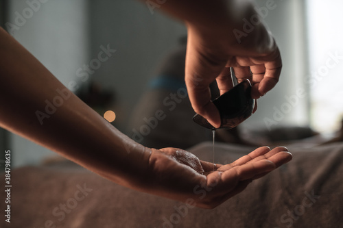 Masseur pouring massage oil, woman lying on background at spa center