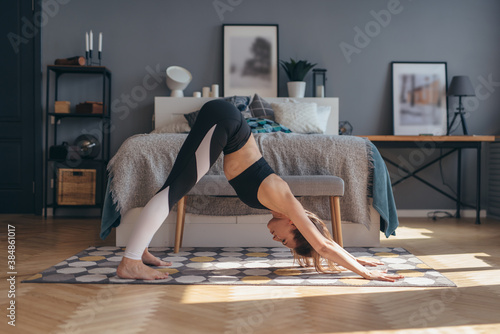 Fit woman doing stretching workout in morning at home. Downward facing dog yoga pose