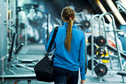 Fit woman in sportswear entering gym, blurred equipment. Young female preparing for training. Concept of fitness