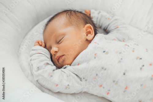 Upper view photo of a caucasian newborn baby sleeping in white clothes at home