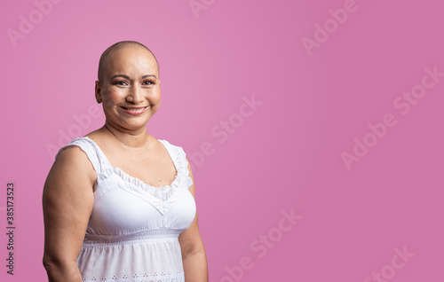 Mujer latina sin cabello con cáncer de mama en un fondo liso color rosa 