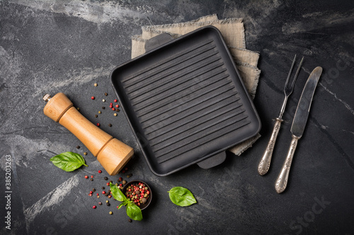 Grill pan with bright spices, basil leaves, pepper mill and silver cutlery for tasty cooking