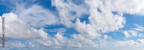 Fluffy cumulus clouds, translucent cirrus and stratus clouds float slowly across the bright blue sky on a sunny day. Panoramic skyscape shot. Weather, meteorology and types of clouds.
