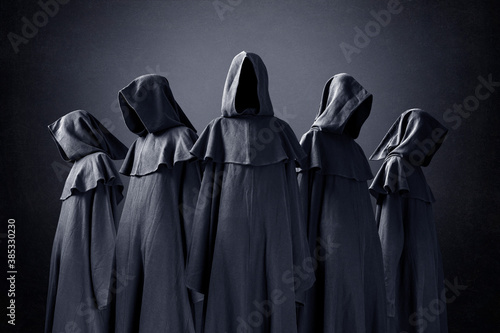 Group of five scary figures in hooded cloaks in the dark