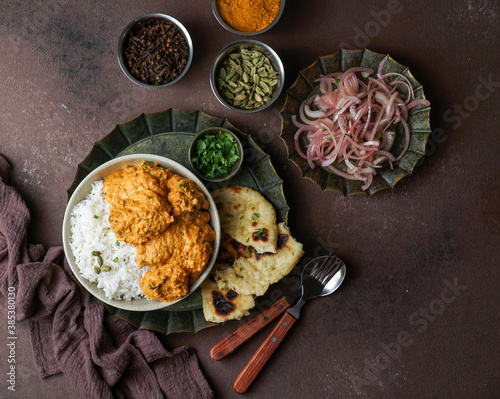 Indian Butter chicken with basmati rice, spices, naan bread. onion salad, Brown background. Space for text