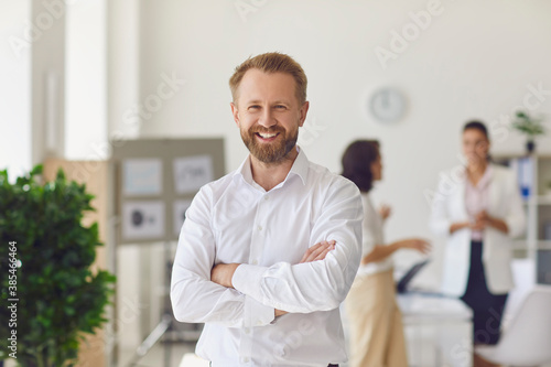 Happy successful businessman or company employee standing in office looking at camera