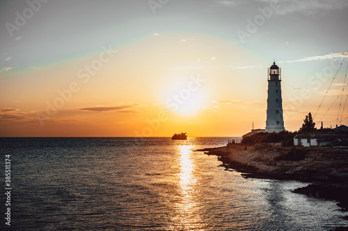 old lighthouse at sunset. a sunken ship in the distance. vertical photo