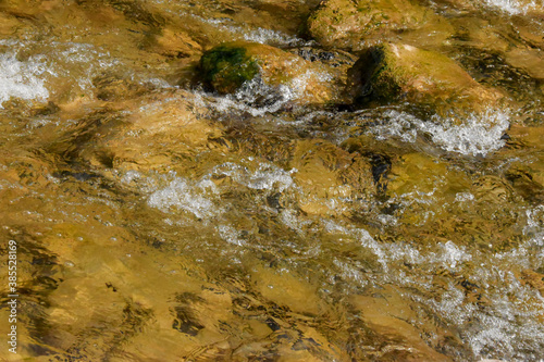 The seething water of the river runs over large and small stones. The water in the river is clear, it runs quickly and the entire bottom is visible.