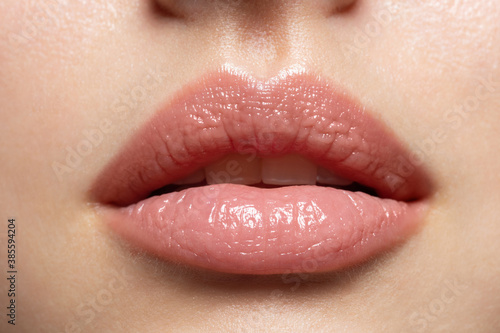 Close up of young woman wearing light fresh lip make up and slightly opening mouth. Plump lips with natural makeup. Part of female face