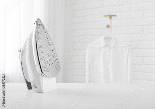 Electric iron on table in blurred room with clothes rack