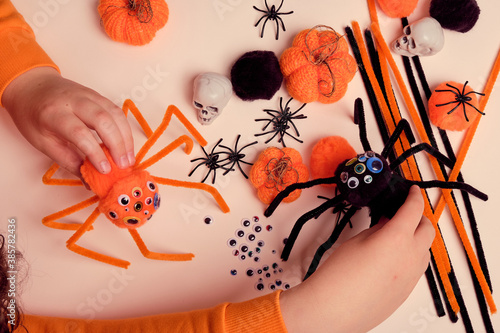 Child makes Halloween decoration and plays with handmade fluffy spiders, bright orange knitted pumpkins, pom poms, pipe cleaners, artificial spiders and skulls . Children craft. Halloween decoration.