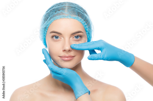 Young woman ready for rhinoplasty, doctor in blue gloves touching her nose, isolated on white background