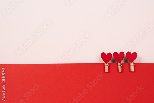 Wooden clothespins with red hearts on a sheet of paper light background