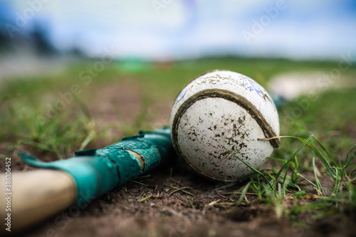 A hurley and a sliothar lie in the grass with a out of focus background