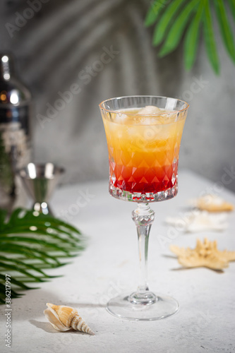 Colourful exotic Tequila Sunrise cocktail in a glass served with ice on gray background
