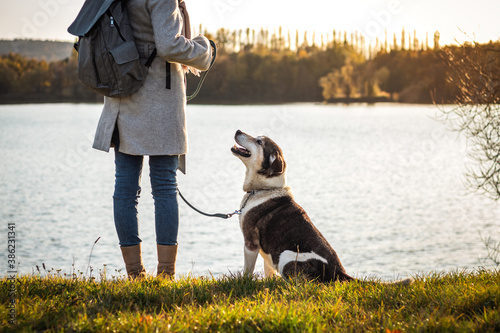 Woman standing with her dog next to lake. Cute dog looking at pet owner